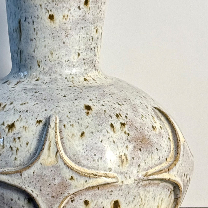 Close up of andcrafted ceramic bud vase with a carved mid-century modern starburst pattern and warm speckled ivory glaze.