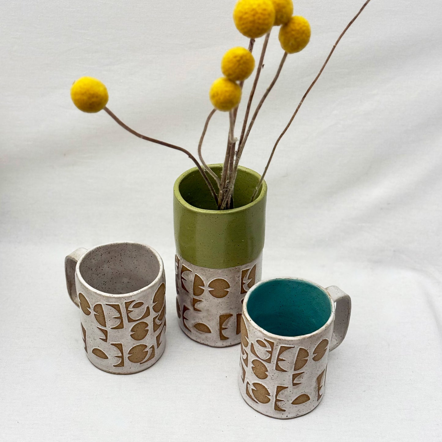 ceramic vase with geometric patterns with two matchings mug behind it on a white background