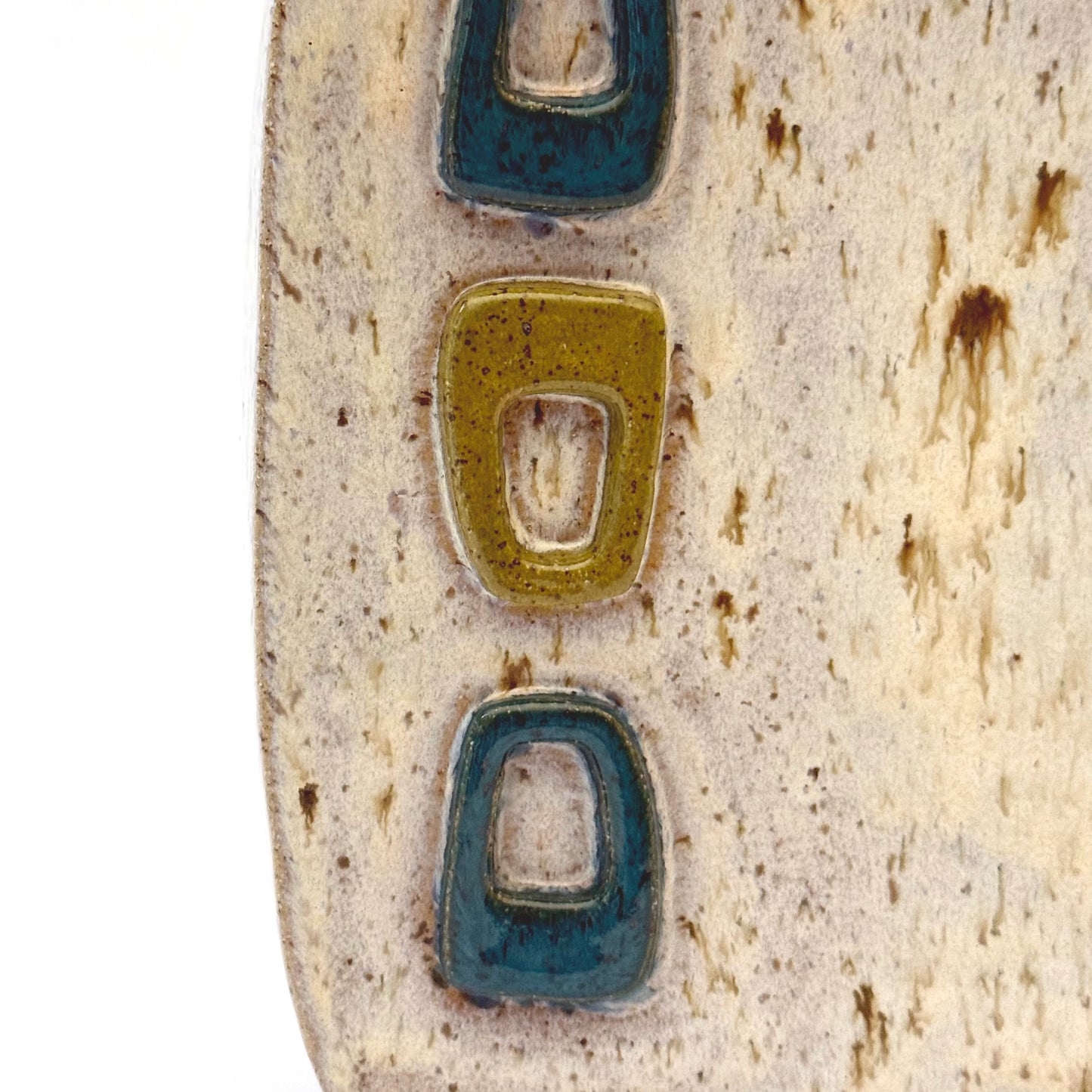 Close up of mid-century modern ceramic vase with three raised turquoise and olive green geometric shapes on a speckled cream stoneware body.