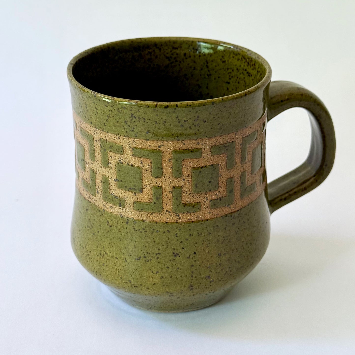 Glossy olive-green speckled mug featuring a contrasting mid-century geometric breeze block pattern.