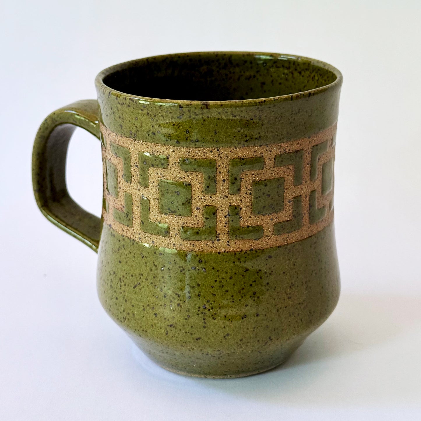 Glossy olive-green speckled mug featuring a contrasting mid-century geometric breeze block pattern.