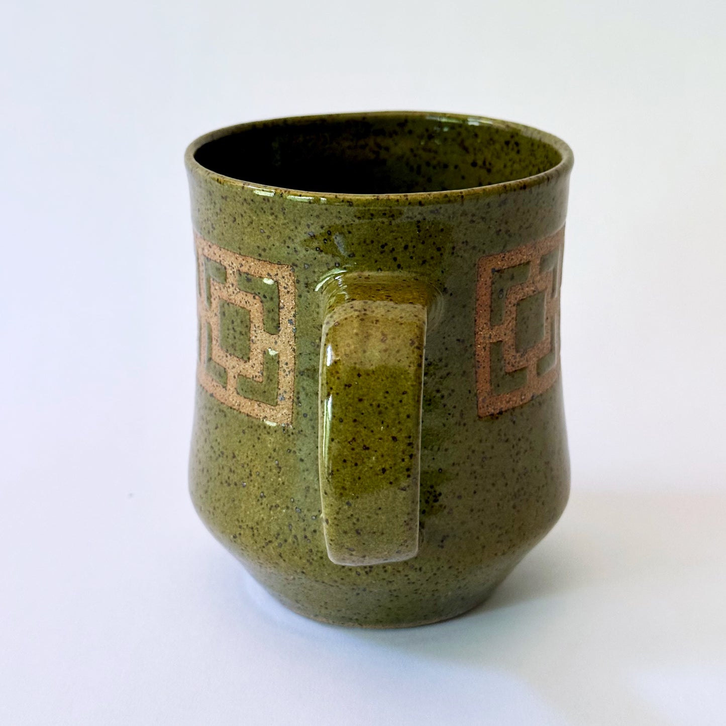 Glossy olive-green speckled mug featuring a contrasting mid-century geometric breeze block pattern.