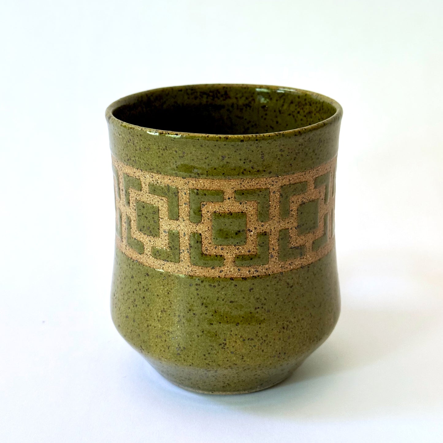 Glossy olive-green speckled mug featuring a contrasting mid-century geometric breeze block pattern.