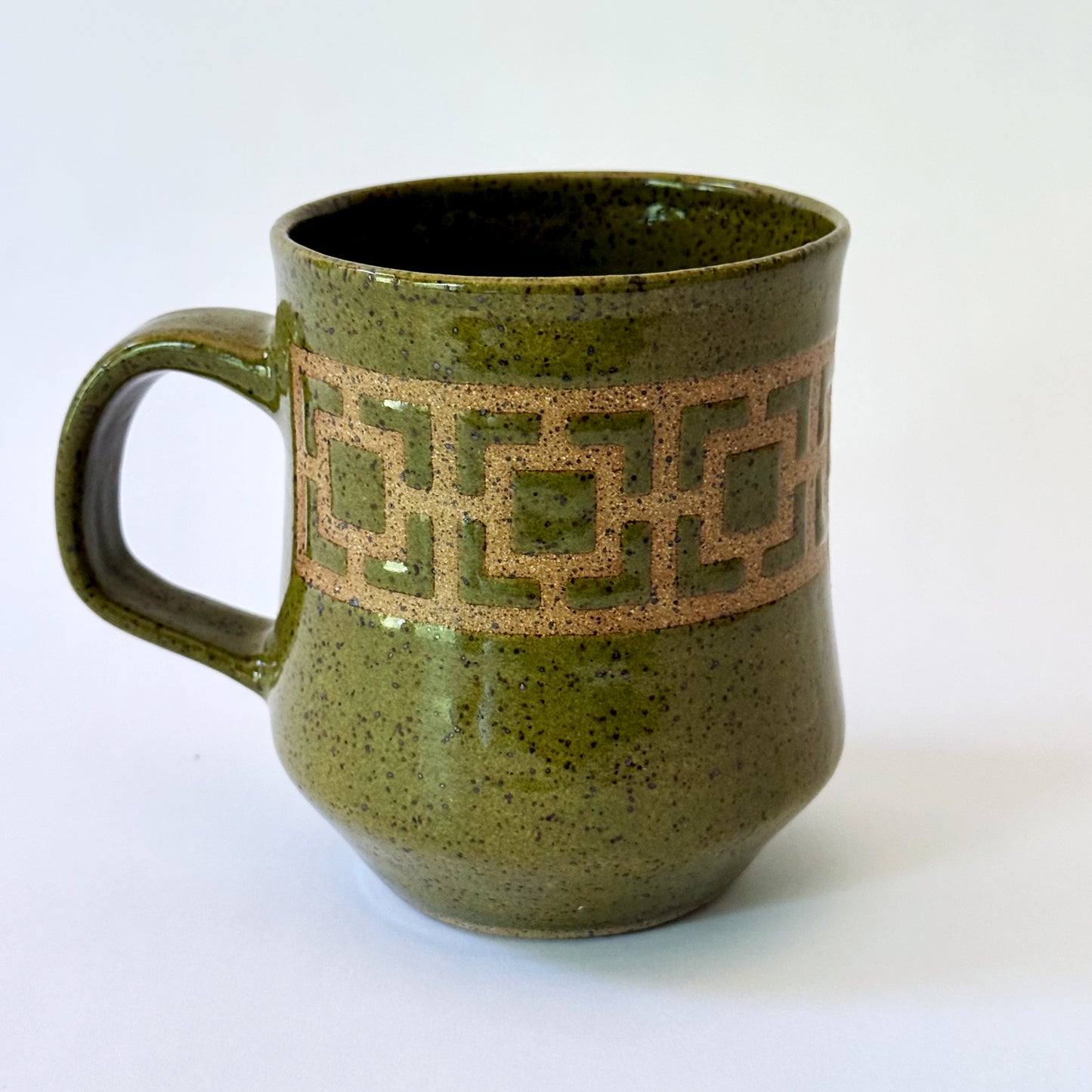 Glossy olive-green speckled mug featuring a contrasting mid-century geometric breeze block pattern.