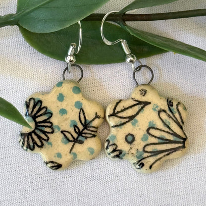 Pair of floral-patterned earrings on a white fabric background with green leaves.