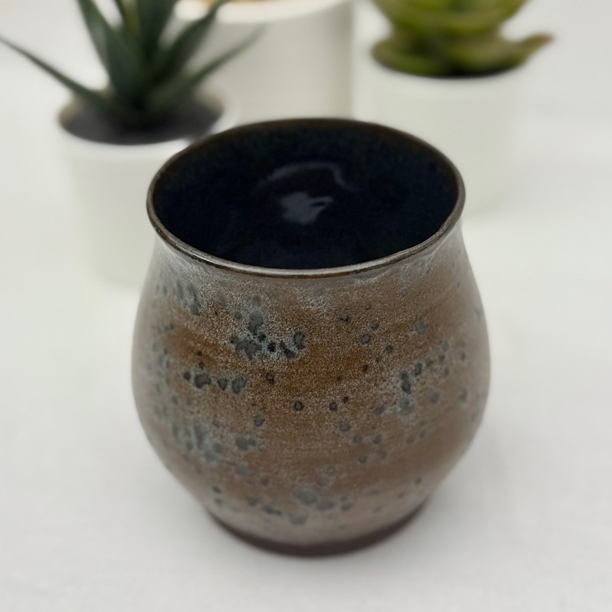 Ceramic cup with speckled design on a white surface with blurred plants in the background