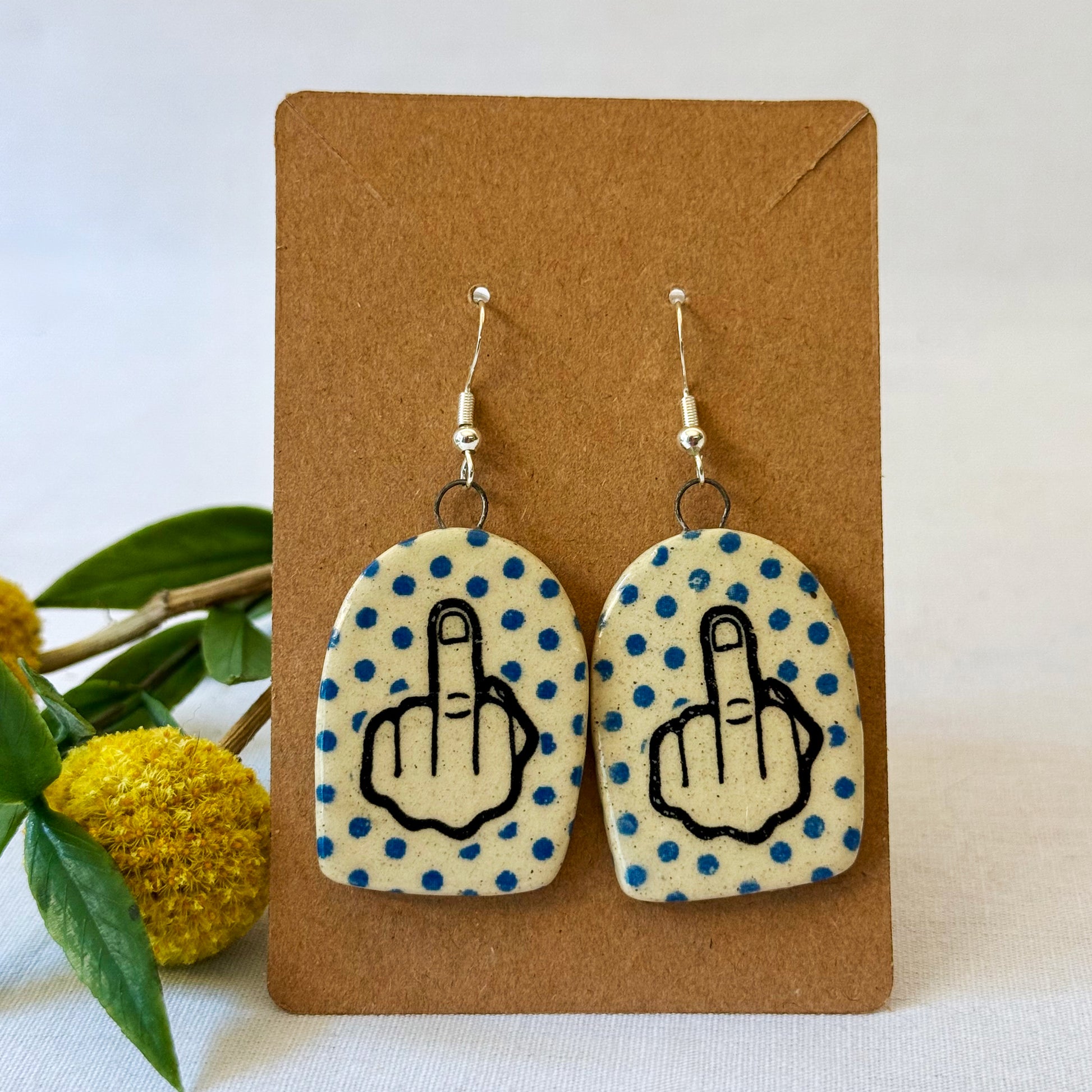 Earrings with middle finger symbol on a brown card 