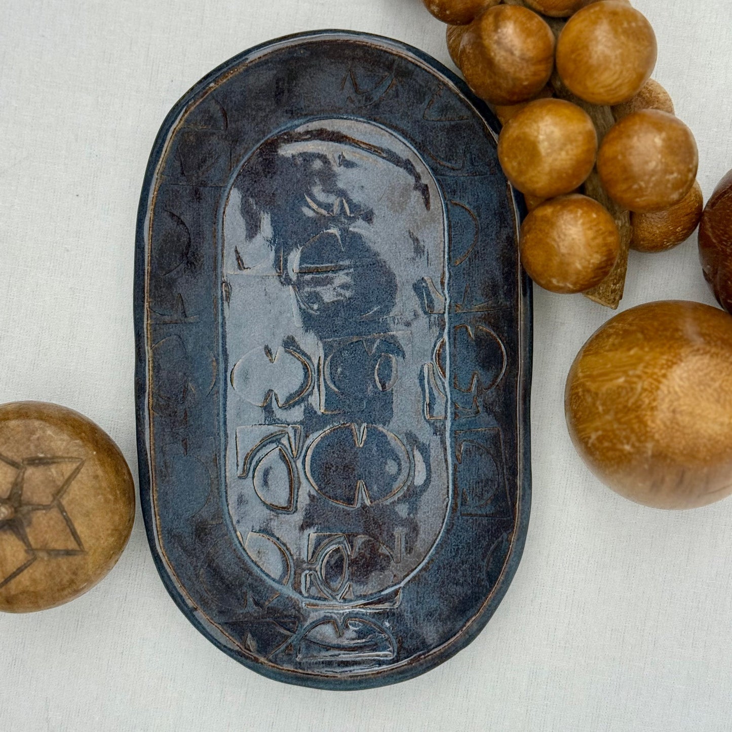ceramic tray with mid century texture surrounded by monkey pod wooden fruit on a light background