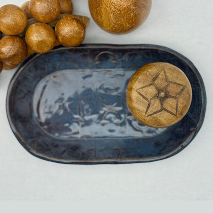 ceramic tray with mid century texture surrounded by monkey pod wooden fruit on a light background