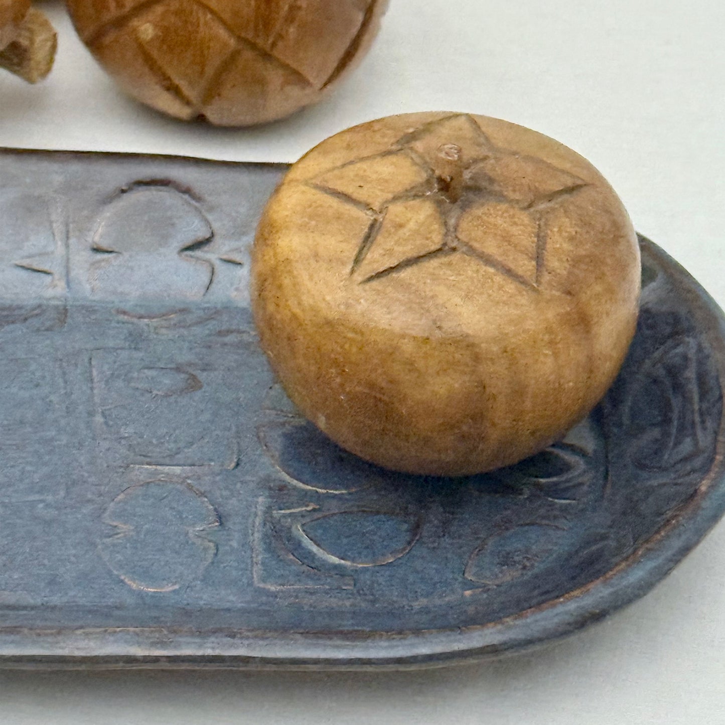 ceramic tray with mid century texture surrounded by monkey pod wooden fruit on a light background
