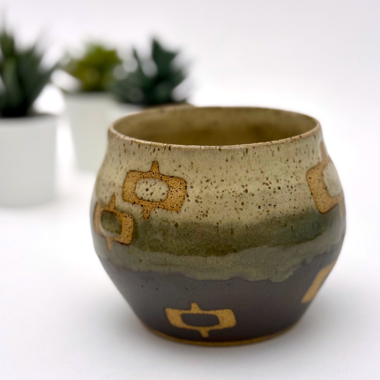 Handmade ceramic mug with a rounded shape, finished in two glazes with a mid-century–inspired pattern in earthy tones.