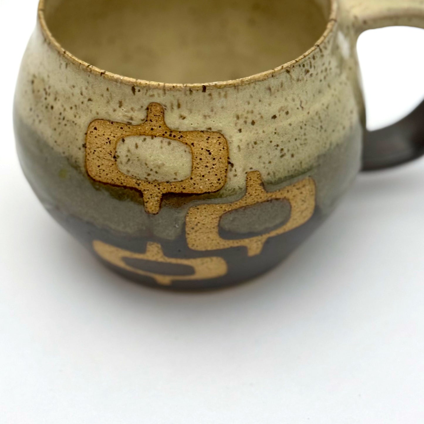 Handmade ceramic mug with a rounded shape, finished in two glazes with a mid-century–inspired pattern in earthy tones.