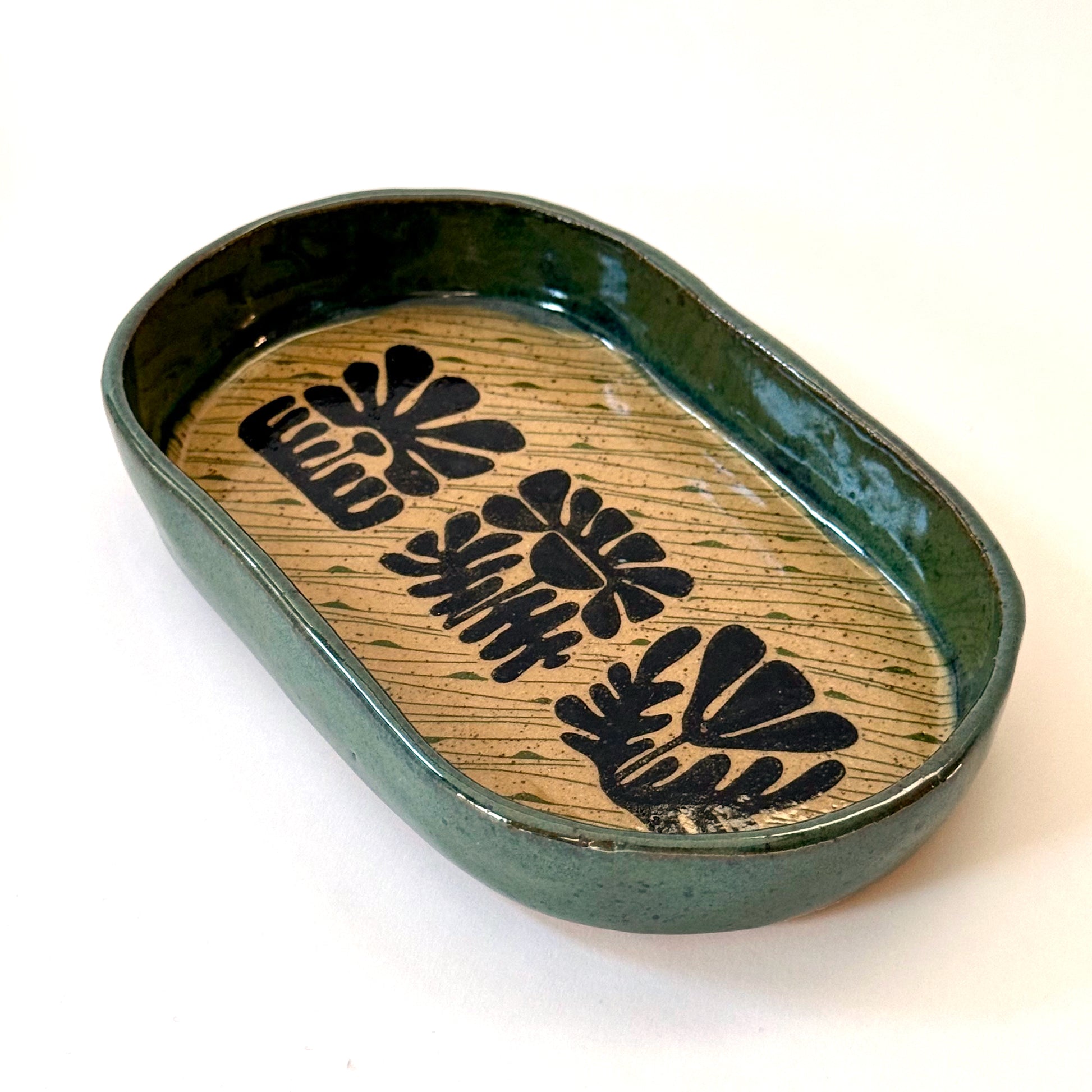 Ceramic dish with green exterior and  interior featuring black floral patterns on a white background