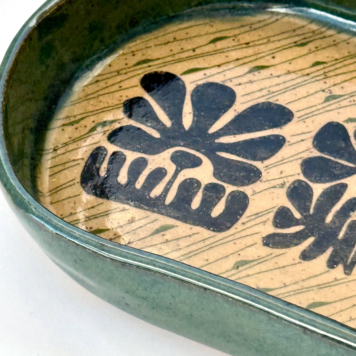 Close up of ceramic dish with floral patterns and green rim on a white background
