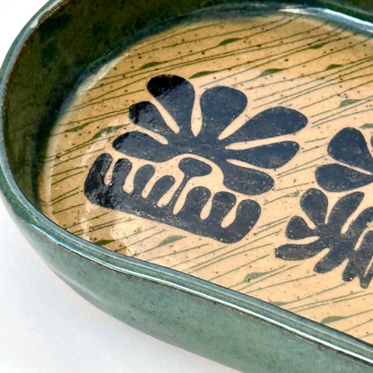 Close up of ceramic dish with floral patterns and green rim on a white background