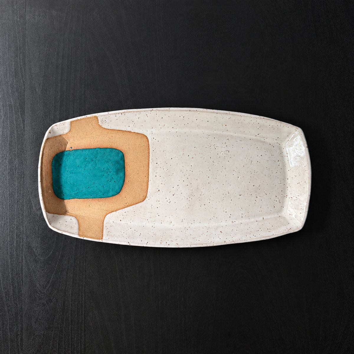 Handmade rectangular ceramic trays with softly rounded corners, finished in a glossy white glaze with exposed speckled clay forming mid-century geometric designs. Accents of turquoise blue, mustard yellow, and olive green add pops of color.