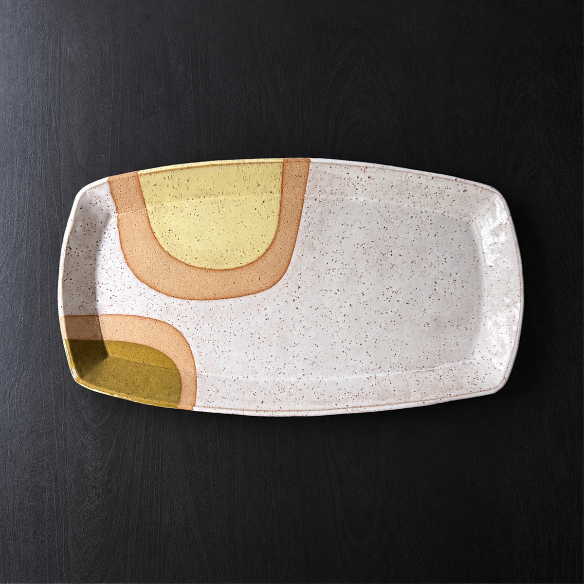 Handmade rectangular ceramic trays with softly rounded corners, finished in a glossy white glaze with exposed speckled clay forming mid-century geometric designs. Accents of turquoise blue, mustard yellow, and olive green add pops of color.