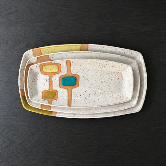 Three handmade rectangular ceramic trays with softly rounded corners, finished in a glossy white glaze with exposed speckled clay forming mid-century geometric designs. Accents of turquoise blue, mustard yellow, and olive green add pops of color across the three different patterns.