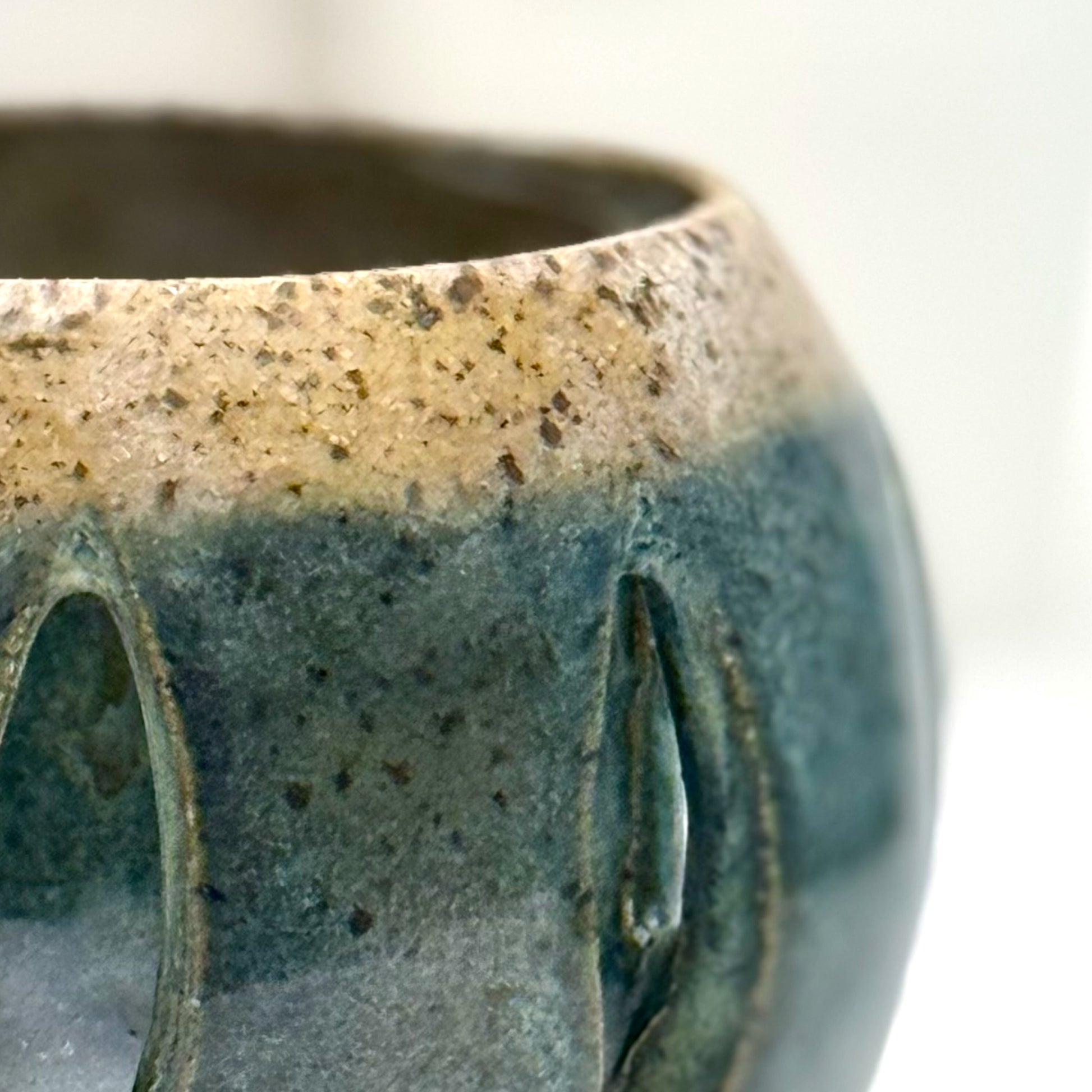 Close-up of a ceramic luminary with teal glaze and vertical cutouts.