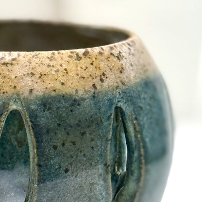 Close-up of a ceramic luminary with teal glaze and vertical cutouts.