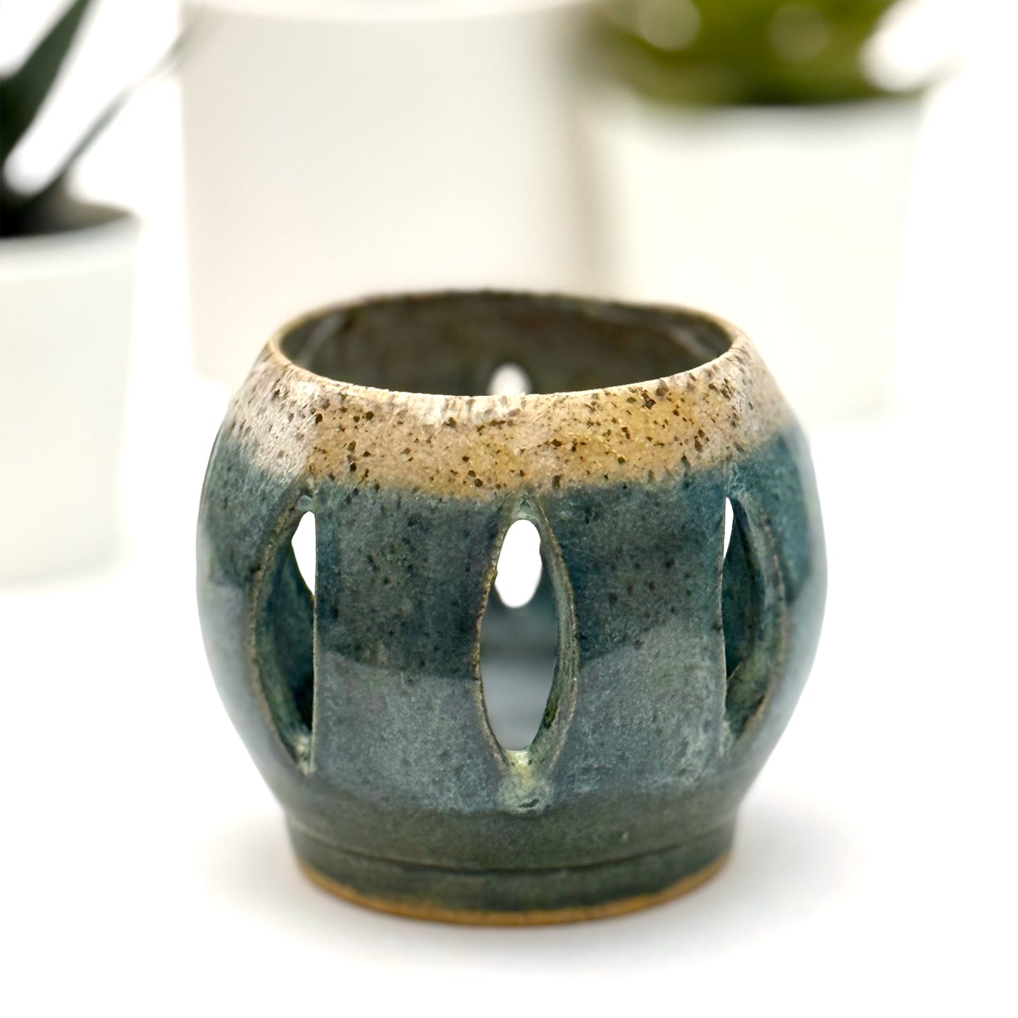 Ceramic luminary with teal glaze and vertical cutouts.