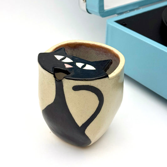 Handbuilt stoneware to go mug with a black cat peeking over the rim, finished with a smooth glaze and hand-painted details.