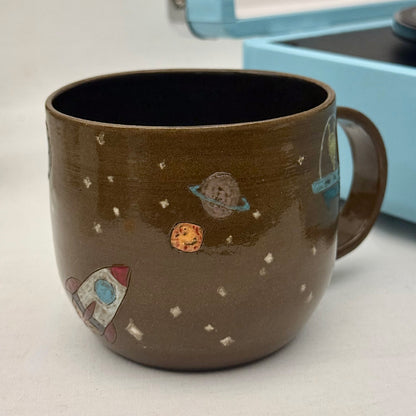 ceramic mug with space-themed decorations on a light surface.