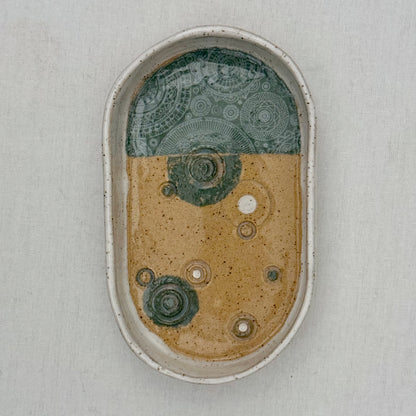 Oval ceramic dish with green and brown design on a light gray background