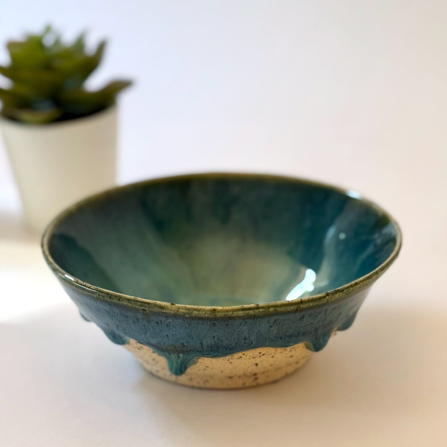 Blue ceramic bowl on a white surface with a blurred plant in the background