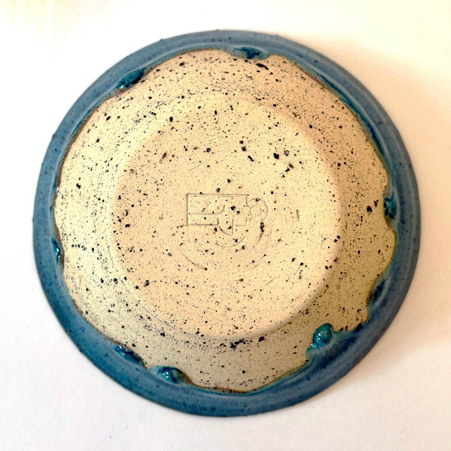 Bottom view of handmade stoneware bowl with blue-green glaze interior and dripped glaze edge over a speckled clay base.