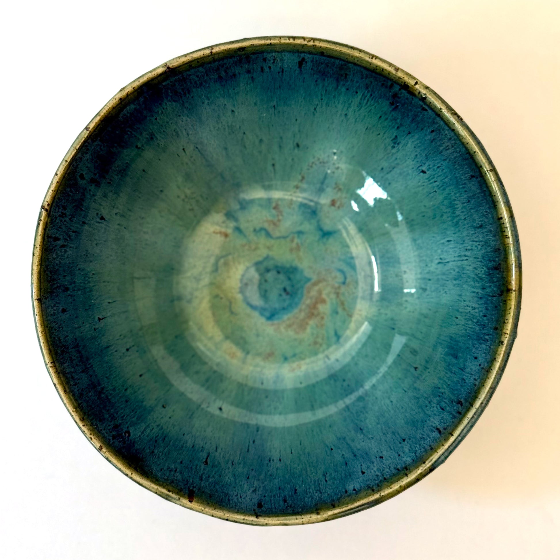 Interior view of handmade stoneware bowl with blue-green glaze interior and dripped glaze edge over a speckled clay base.