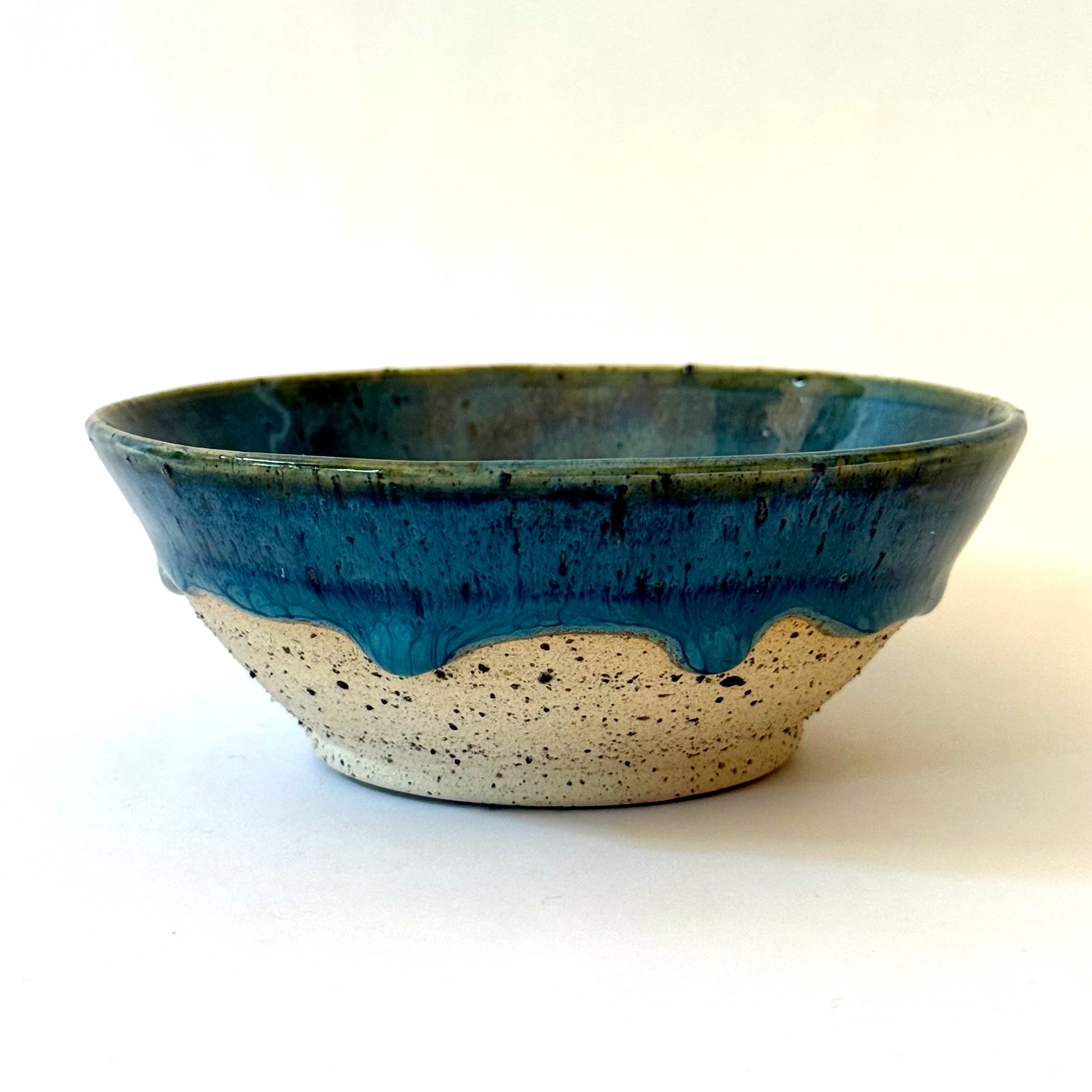 Handmade stoneware bowl with blue-green glaze interior and dripped glaze edge over a speckled clay base.