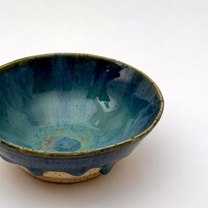 Handmade stoneware bowl with blue-green glaze interior and dripped glaze edge over a speckled clay base.