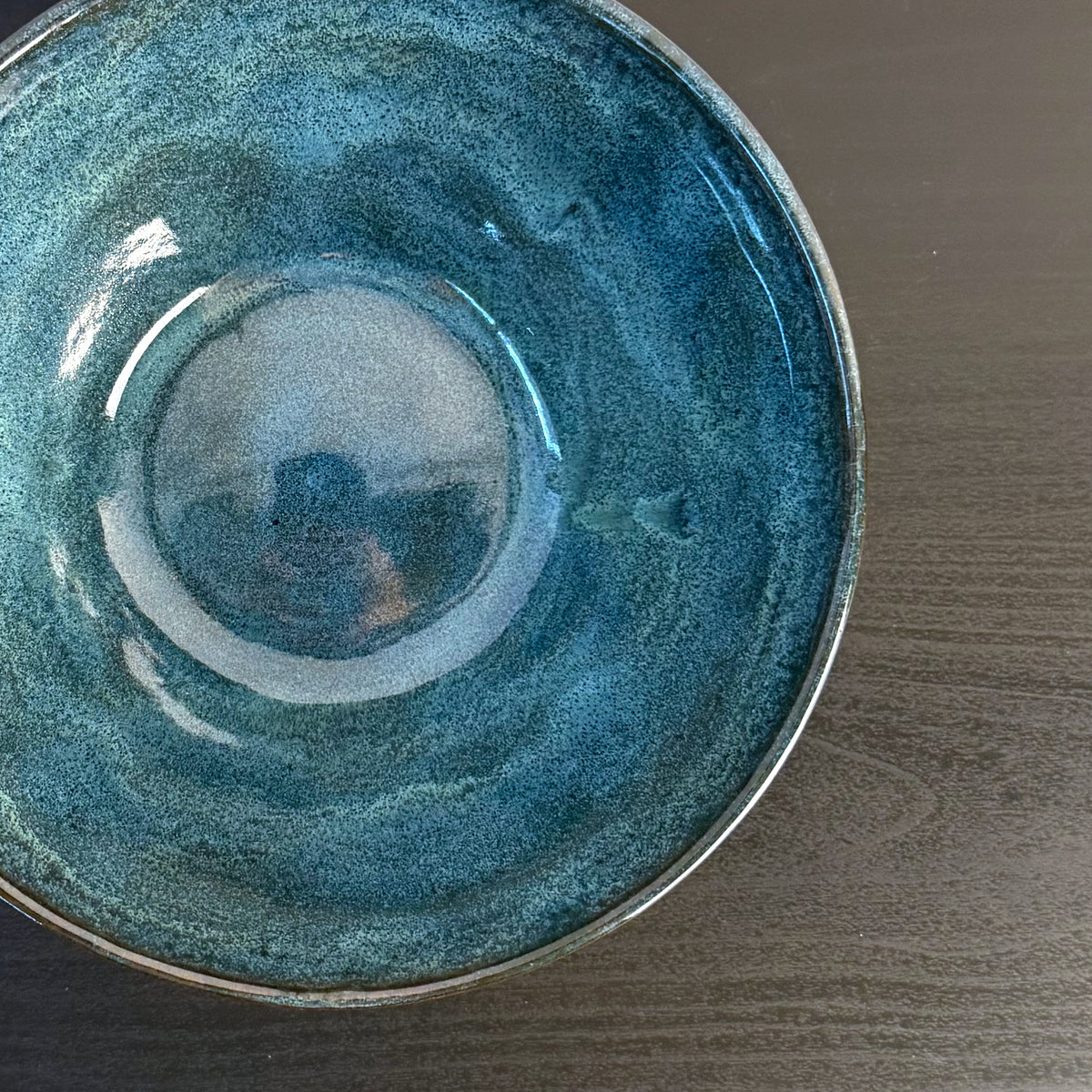 Handmade ceramic bowl with a glossy deep teal glaze, subtle blue-green variation, and a band of exposed natural clay around the base.