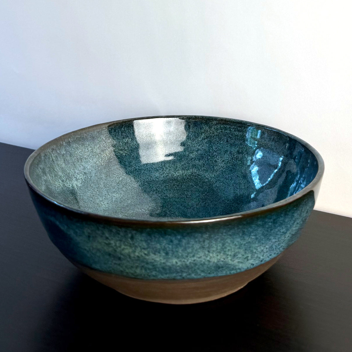 Handmade ceramic bowl with a glossy deep teal glaze, subtle blue-green variation, and a band of exposed natural clay around the base.