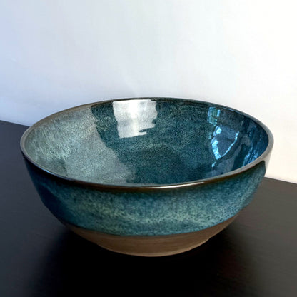 Handmade ceramic bowl with a glossy deep teal glaze, subtle blue-green variation, and a band of exposed natural clay around the base.