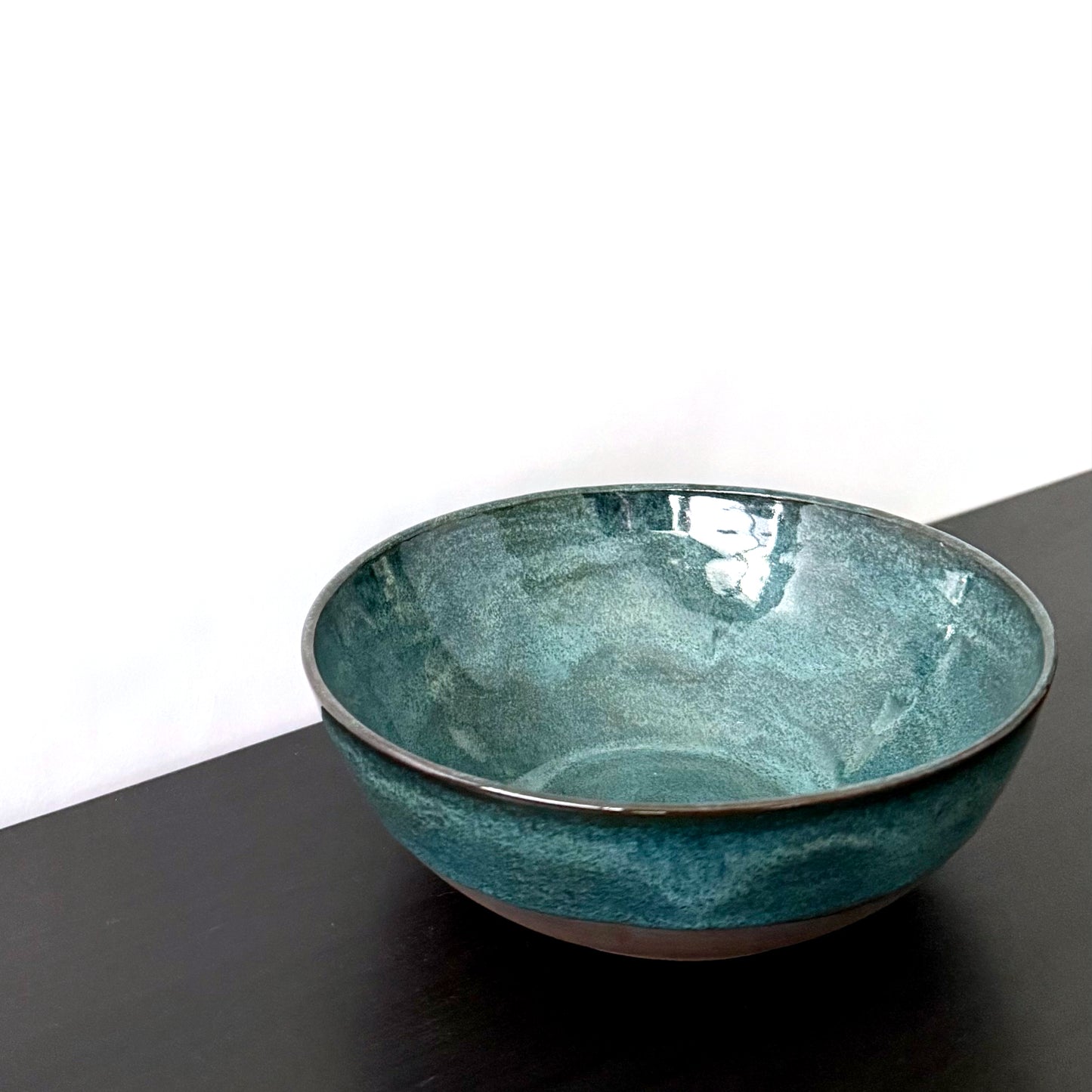 Handmade ceramic bowl with a glossy deep teal glaze, subtle blue-green variation, and a band of exposed natural clay around the base.