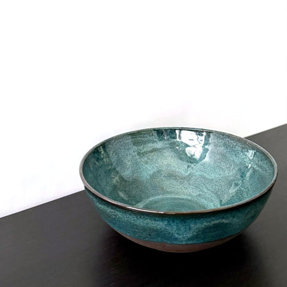 Handmade ceramic bowl with a glossy deep teal glaze, subtle blue-green variation, and a band of exposed natural clay around the base.