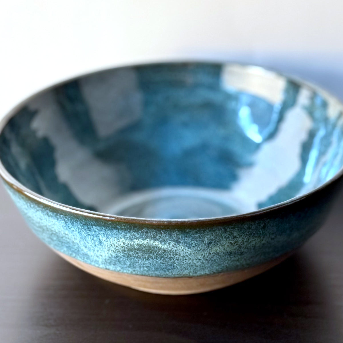 Handmade ceramic bowl with a glossy deep teal glaze, subtle blue-green variation, and a band of exposed natural clay around the base.