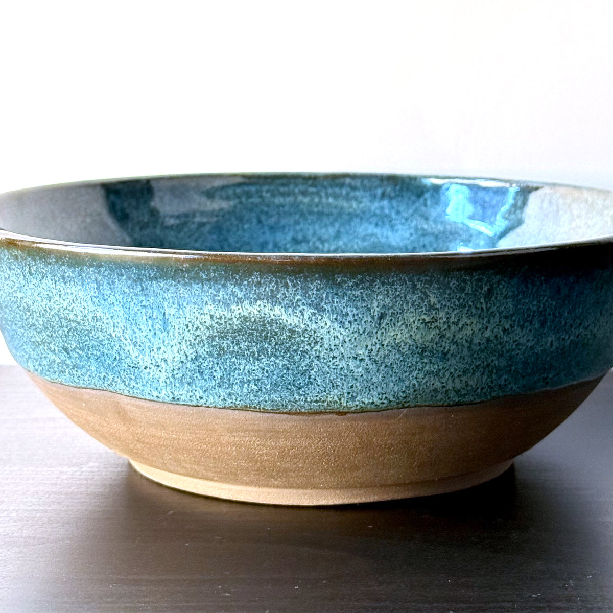 Handmade ceramic bowl with a glossy deep teal glaze, subtle blue-green variation, and a band of exposed natural clay around the base.