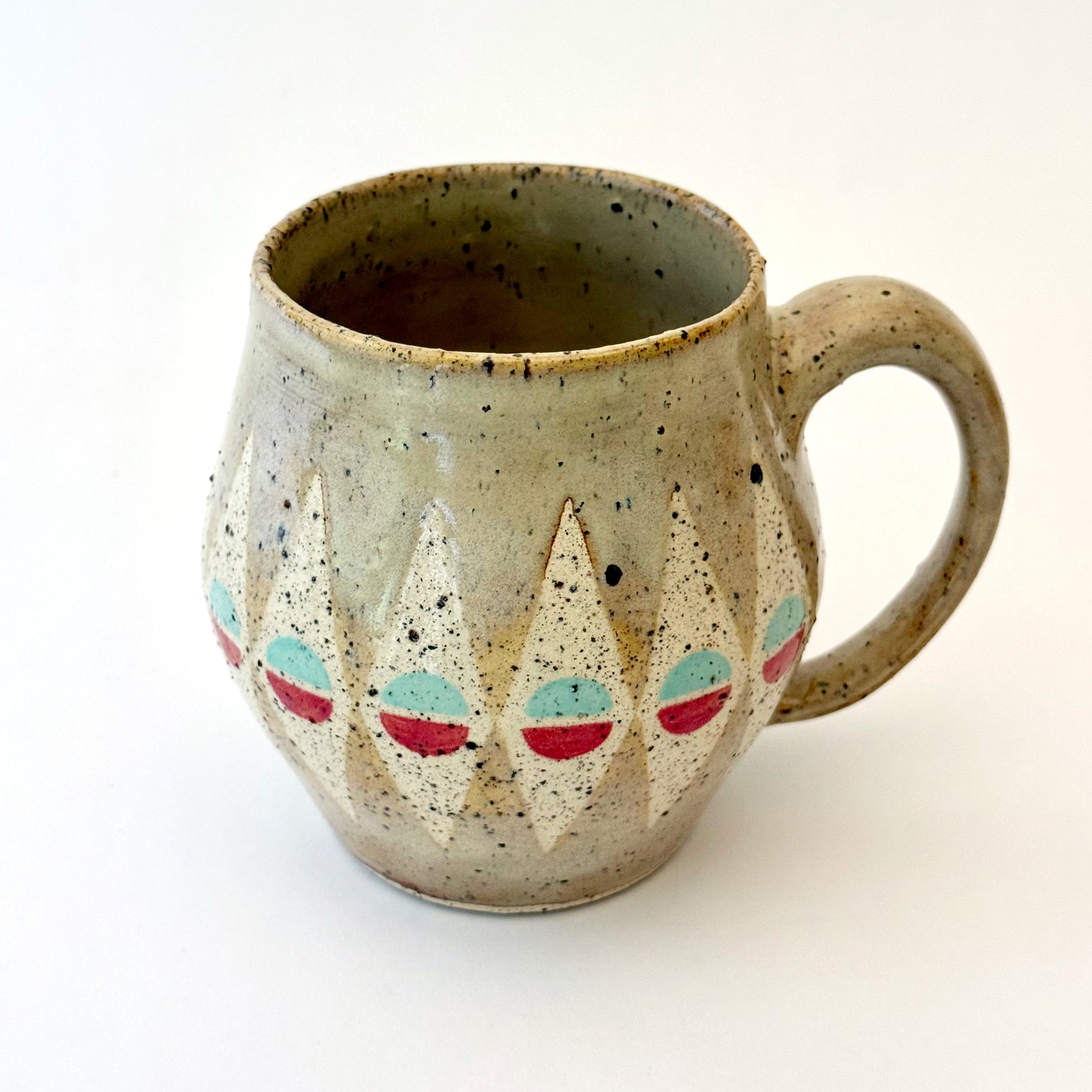 A bell-shaped, speckled tan stoneware mug featuring a pattern of cream diamonds. Each diamond contains a circular motif split into teal and poppy red. The mug has a large, rounded handle and visible dark mineral flecks.