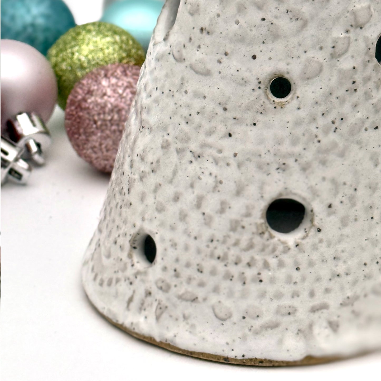 Close-up of a white speckled ceramic tree-shaped luminary with light openings, styled among colorful holiday ornaments.