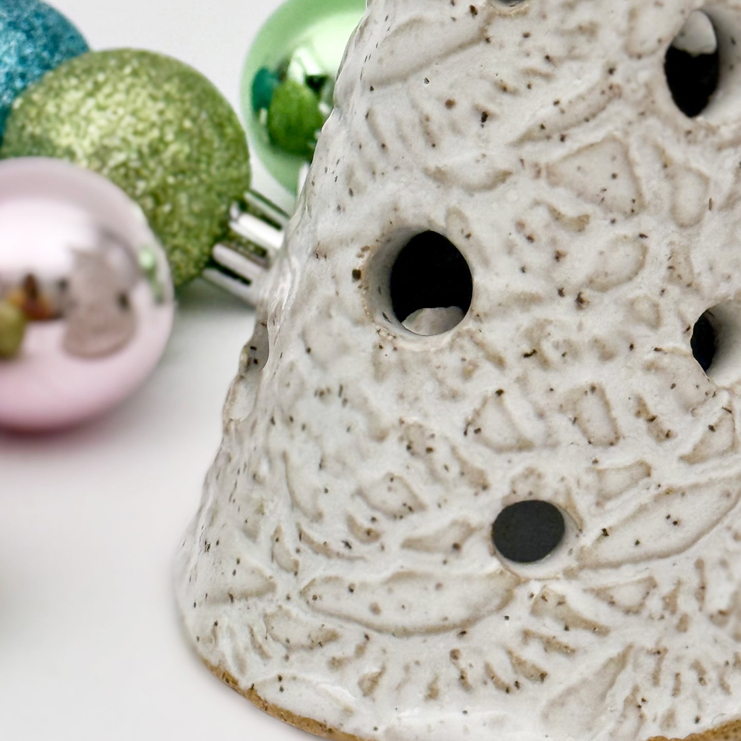 close-up of Textured ceramic tree luminary with decorative Christmas balls in the background