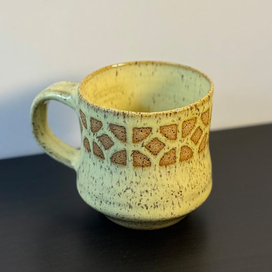 Handmade ceramic mug with a warm yellow glaze, featuring an empress breeze-block pattern around the upper half. The design reveals the natural clay beneath, giving the mug a retro mid-century architectural look.