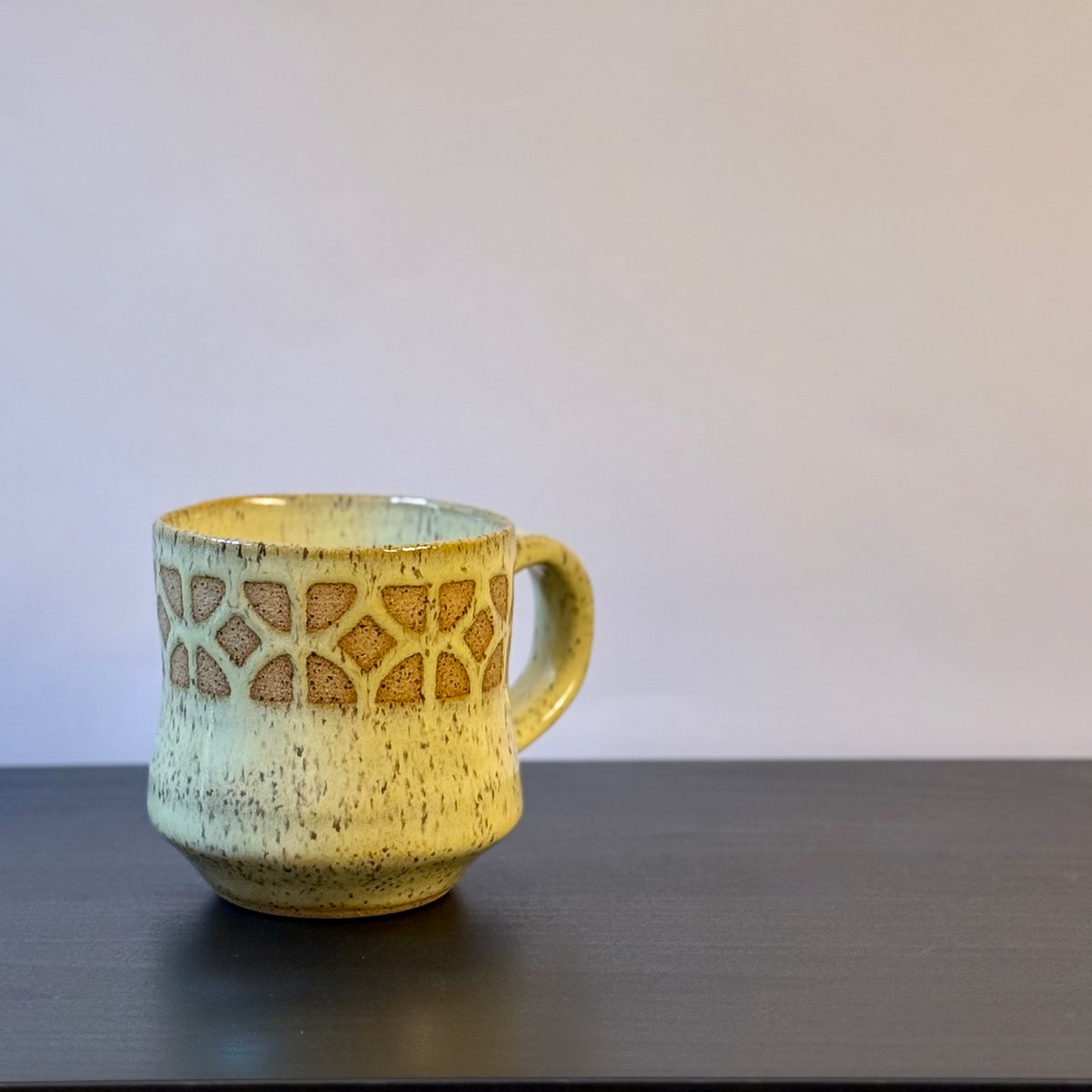 Handmade ceramic mug with a warm yellow glaze, featuring an empress breeze-block pattern around the upper half. The design reveals the natural clay beneath, giving the mug a retro mid-century architectural look.