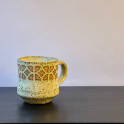 Handmade ceramic mug with a warm yellow glaze, featuring an empress breeze-block pattern around the upper half. The design reveals the natural clay beneath, giving the mug a retro mid-century architectural look.