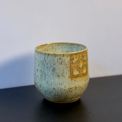Handmade ceramic tumbler with a rounded shape and warm, yellow glaze. A square Empress breeze-block motif is inset on the front, revealing the natural clay and adding a mid-century geometric detail.