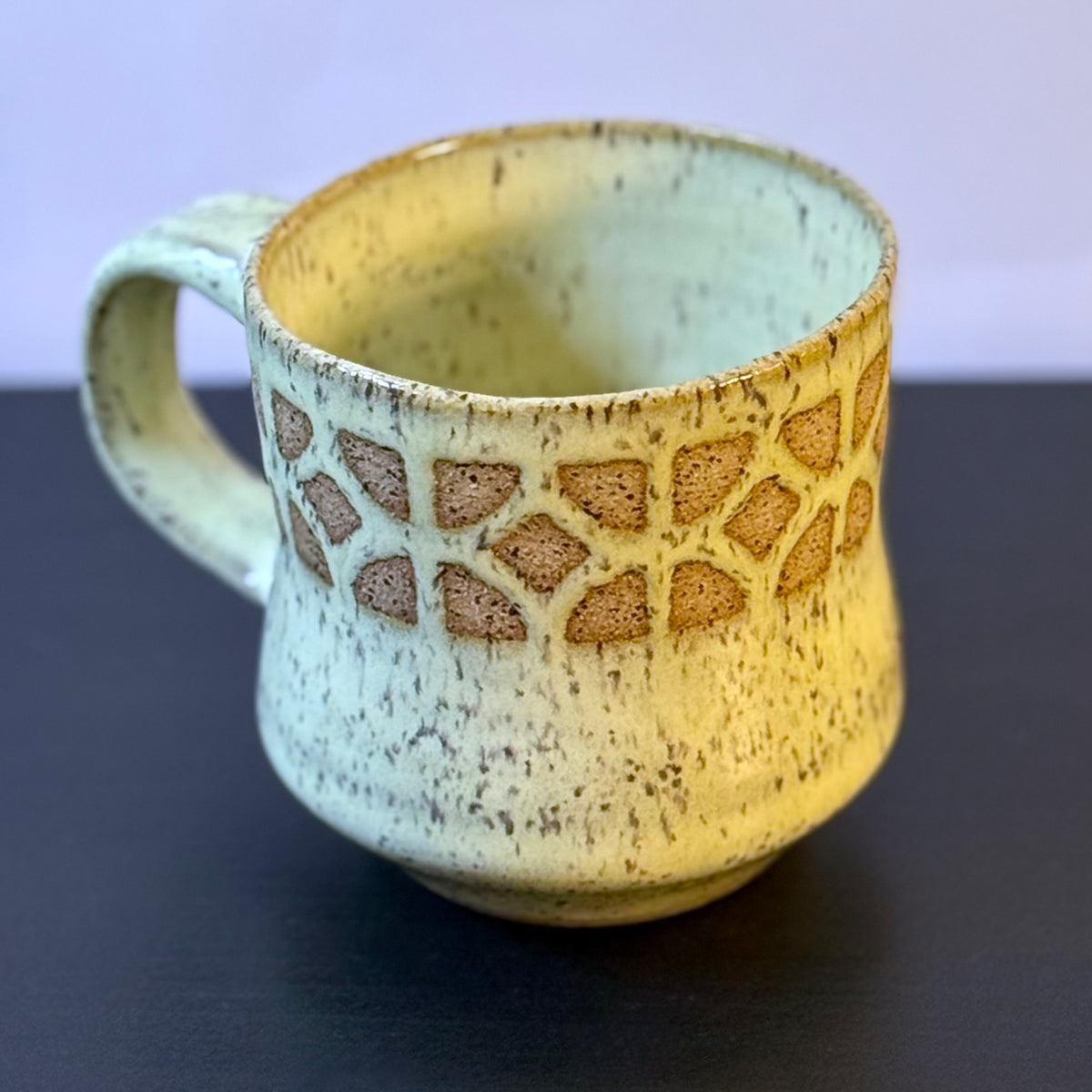 Handmade ceramic mug with a warm yellow glaze, featuring an empress breeze-block pattern around the upper half. The design reveals the natural clay beneath, giving the mug a retro mid-century architectural look.