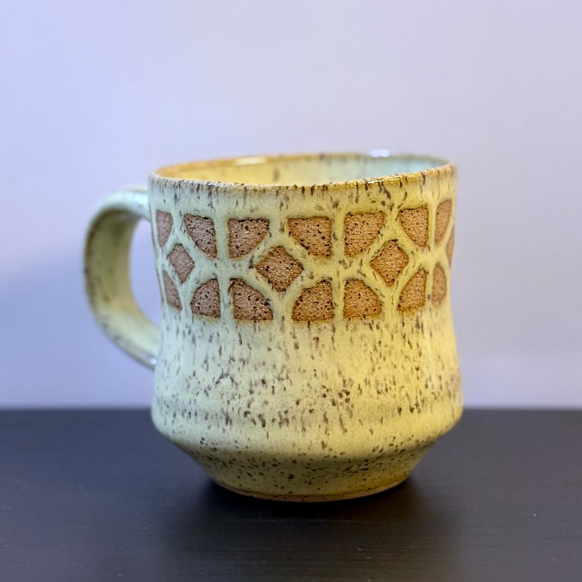 Handmade ceramic mug with a warm yellow glaze, featuring an empress breeze-block pattern around the upper half. The design reveals the natural clay beneath, giving the mug a retro mid-century architectural look.
