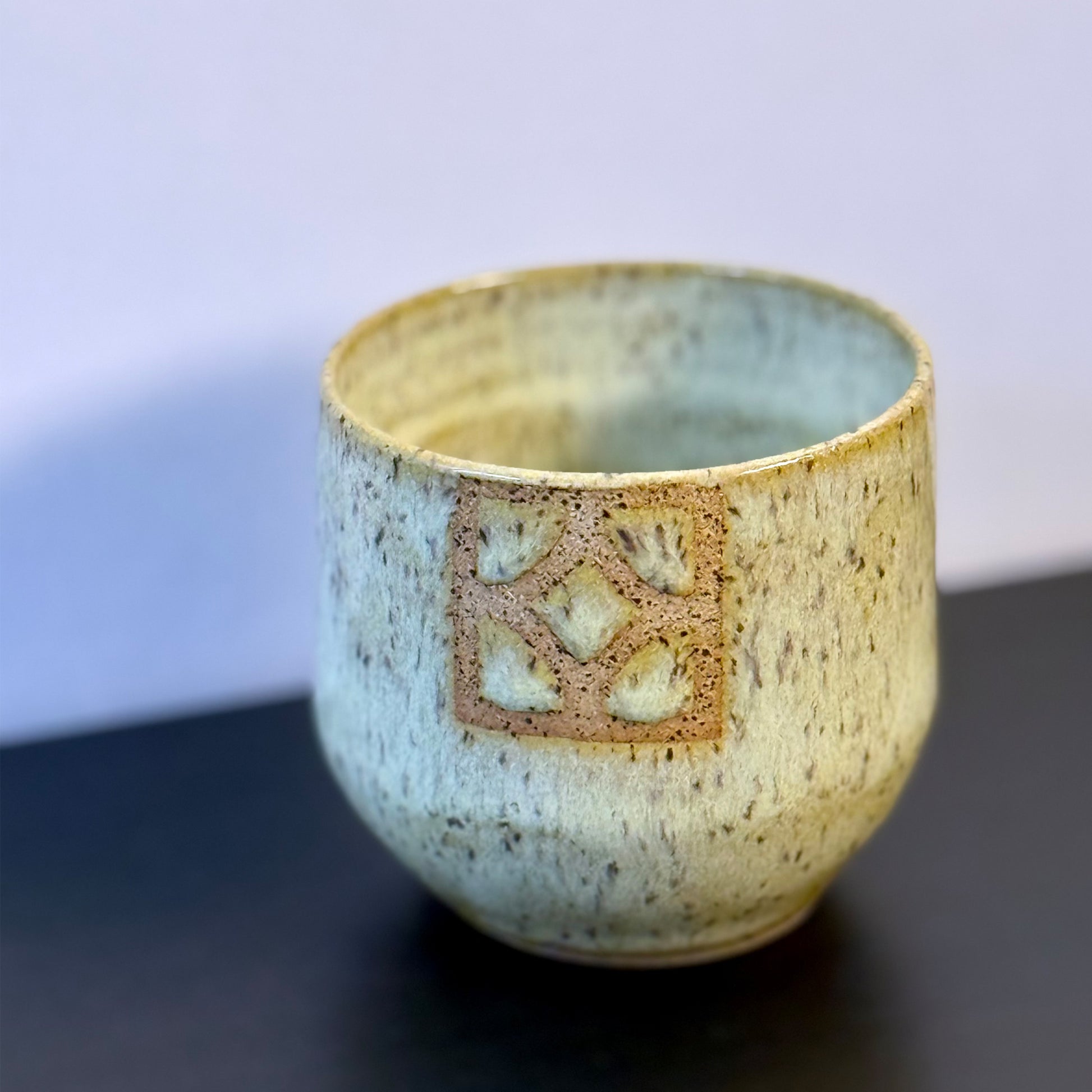 Handmade ceramic tumbler with a rounded shape and warm, yellow glaze. A square Empress breeze-block motif is inset on the front, revealing the natural clay and adding a mid-century geometric detail.